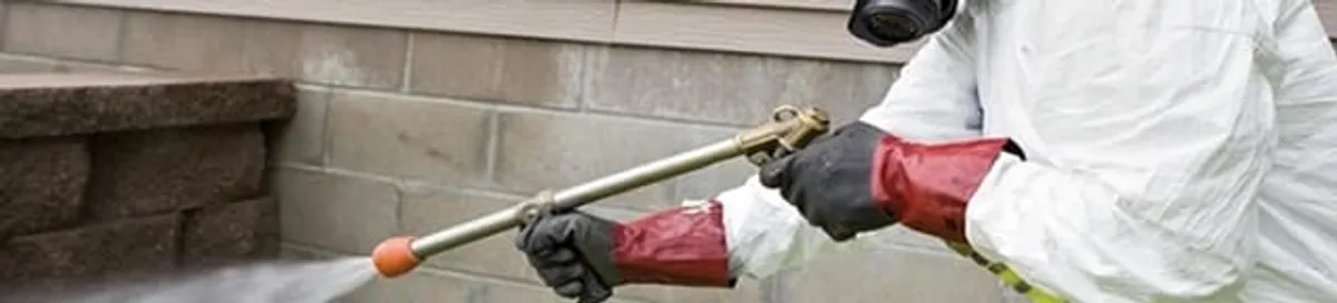 Pest control technician applying exterior insect treatment along a home foundation in Sioux Falls, SD