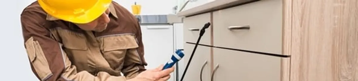 Roach exterminator applying treatment under kitchen cabinets in Sioux Falls, SD
