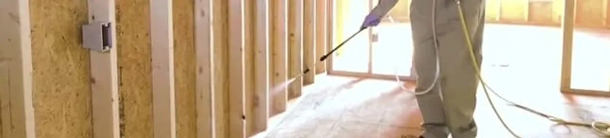 Termite treatment technician applying spray along framing and unfinished walls in Sioux Falls, SD